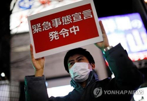 일본 수도권 일부 지역에 코로나19 긴급사태가 발효한 지난달 8일 오후 도쿄도 직원이 신주쿠(新宿)구의 유흥가에서 '긴급사태선언 발령 중'이라고 적힌 안내판을 들고 있다. 도쿄 로이터=연합뉴스